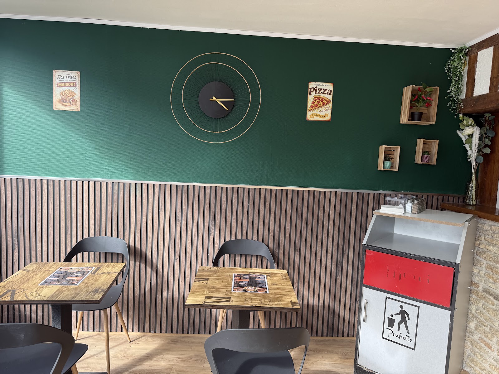 Intérieur du restaurant avec murs verts, horloge dorée et tables en bois